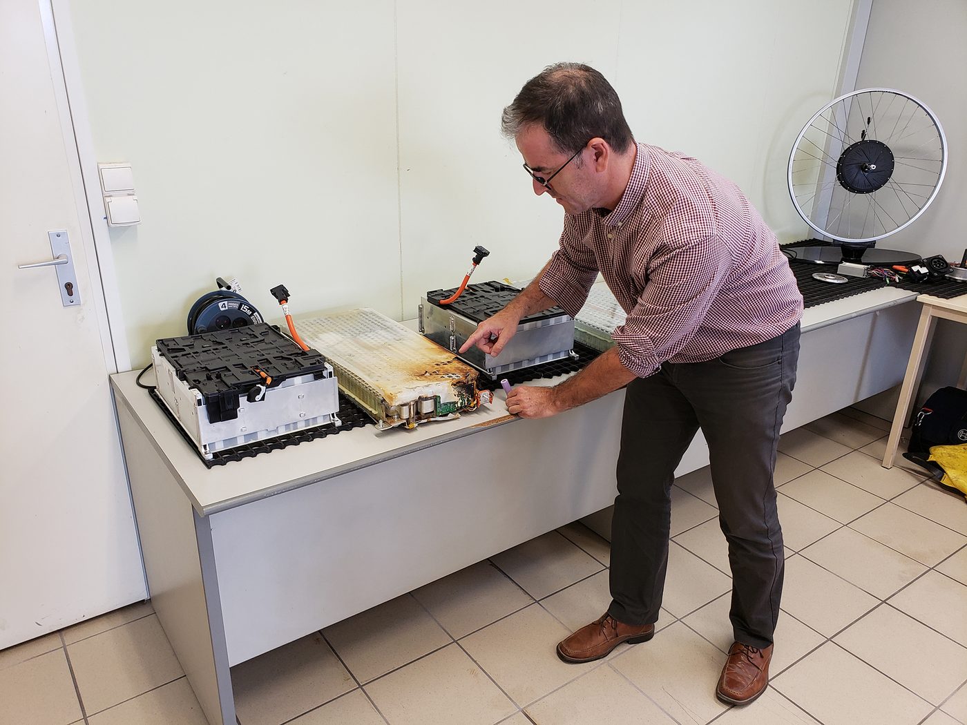 Le formateur désigne l’intérieur d’un module de batterie de traction démonté, dont une partie a brûlé, posé sur une table d’atelier.