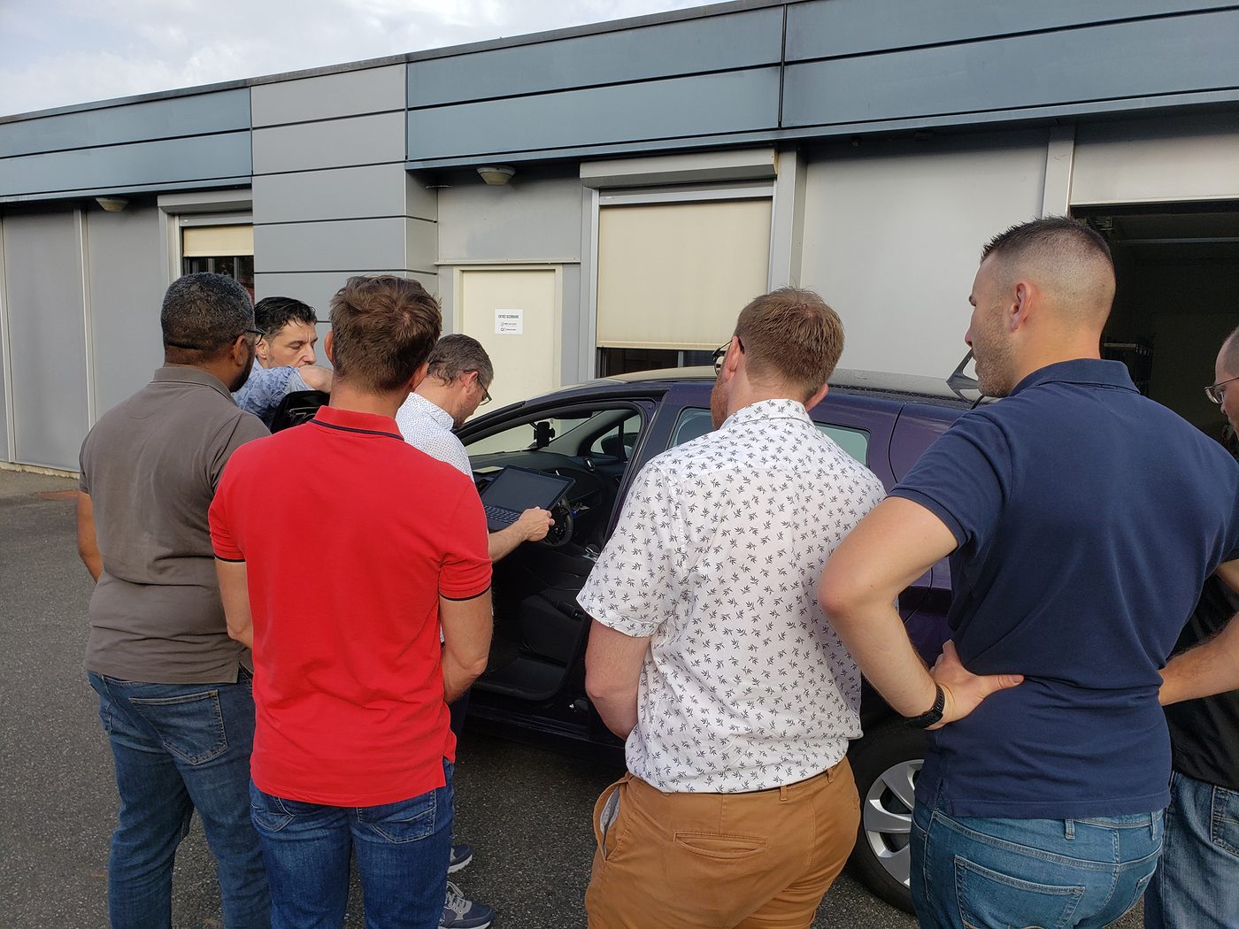 Un groupe de stagiaires réunis autour d’un véhicule électrique, devant un ordinateur portable posé au poste de conduite.